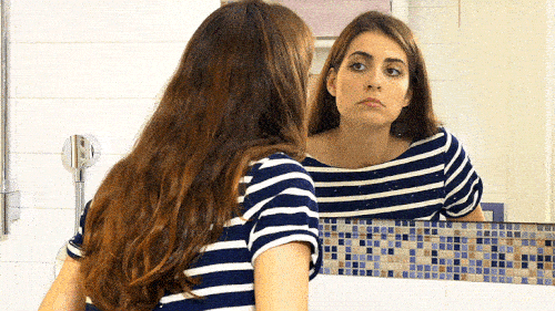 GIF de una chica horrorizada frente al espejo mirando un grano en su cara - Saba