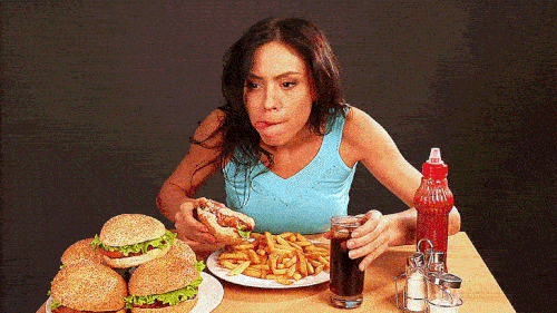 GIF de una chica con antojos y comiendo dos hamburguesas y papa fritas - Libresse